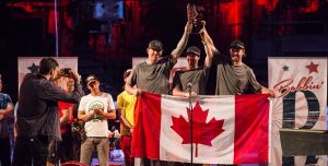 Trois personnes avec des drapeaux canadiens lèvent un trophée.