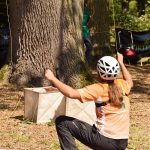 Frau mit Helm zieht an dünnen Seilen die einen Baum gehen