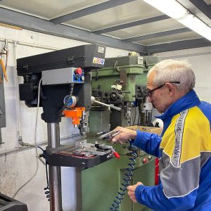 Älterer Herr mit Druckluftpistole in der Hand an einer Standbohrmaschine