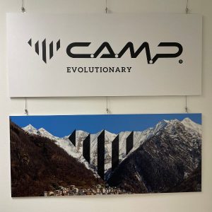 Bild von zwei Tafeln, die oben zeigt das seit 2022 gültige C.A.M.P. Logo, die darunter die Bergkette, die dem Poktogramm als Vorlage diente, als bearbeitetes Foto,