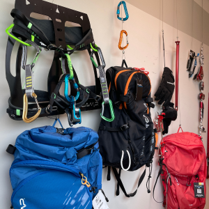 C.A.M.P. Klettergurt, Express-Schlingen, Rucksäcke, Eisschrauben, Handschuhe zur Ausstellung an einer Wand hängen